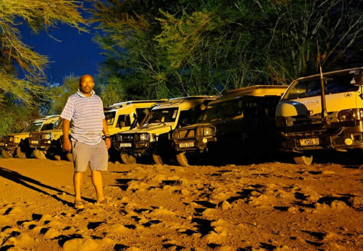 Expert Driver-Guides for Off the Beaten Tracks Safaris Professional safari driver-guide standing at night beside multiple tour Land Cruisers on an off the beaten tracks safari in Kenya