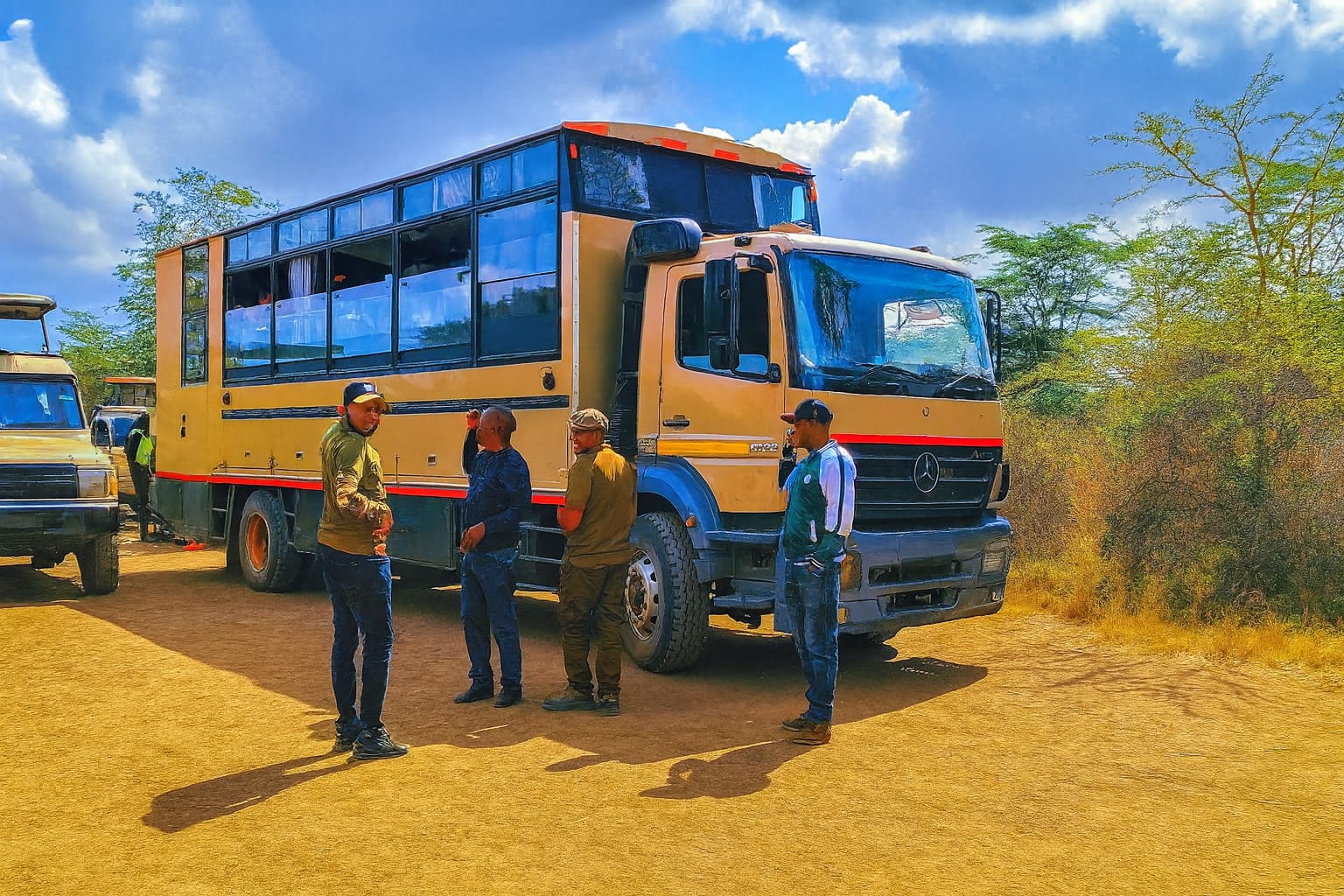 Affarble Overland mobile camping safari truck with guides preparing for departure in a sunny savannah setting.