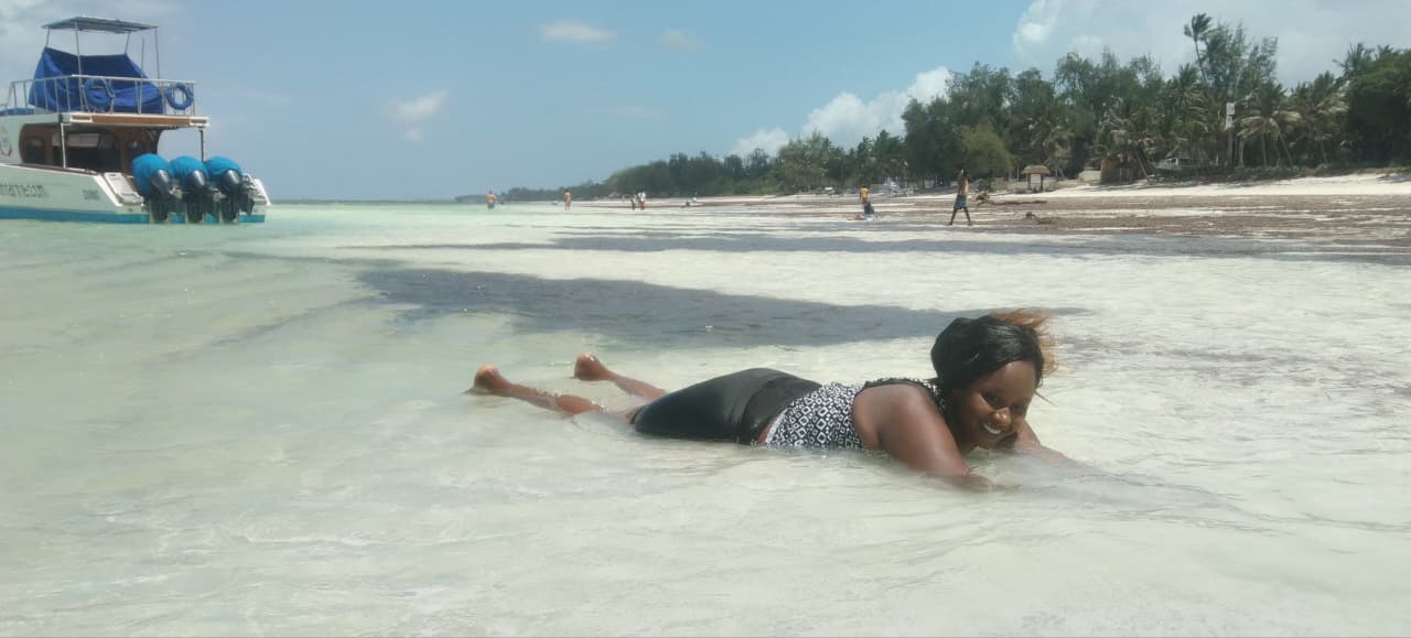 Woman relaxing on a pristine Kenyan beach with a speedboat in the background during a coastal safari experience.